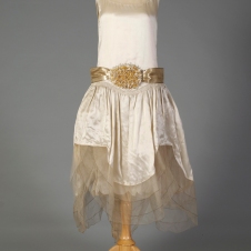 American, ca. 1928. This is a wedding dress, typical of the 1920s it is not floor length and has the addition of artificial orange blossoms on the belt and shoulders.