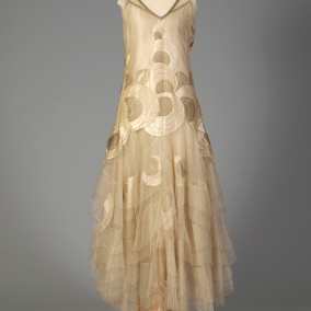 American, ca. 1928-1929. Cream net dress, sleeveless, gold embroidered trim, appliqued with cream and gold embroidery circle designs, graduated petal skirt layers edge with gold thread, attached charmeuse slip.
